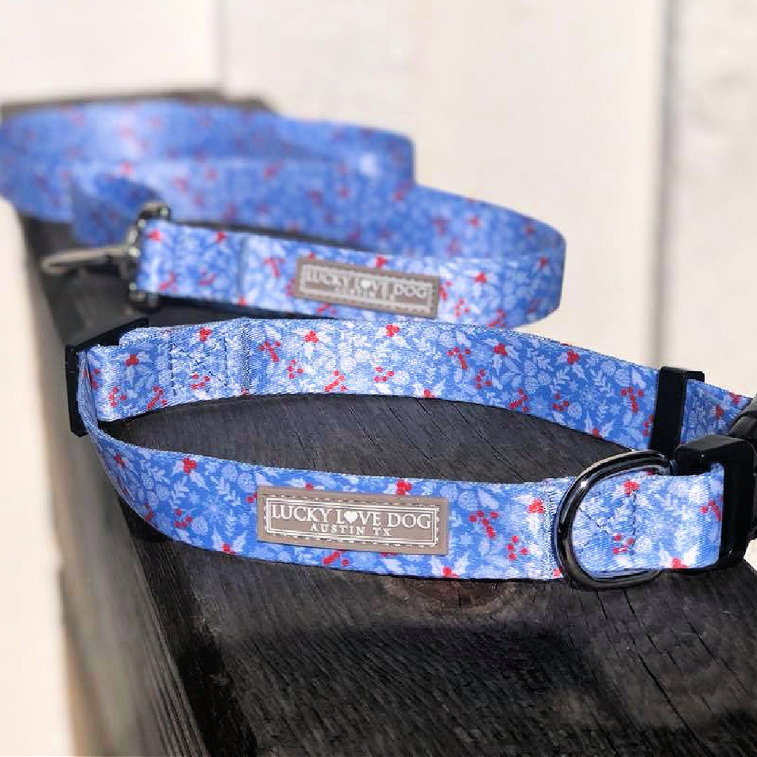 Light blue winter-themed Lucky Love Dog collar and leash with snowflake and berry pattern displayed on a wooden surface.