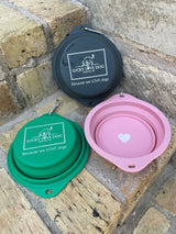 Three collapsible silicone dog bowls in green, pink, and grey resting on stone steps, featuring Lucky Love Dog branding.