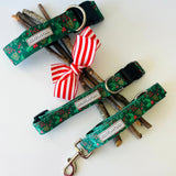 Green holiday-themed Lucky Love Dog collars and leash displayed with festive sticks and a red-and-white striped bow.