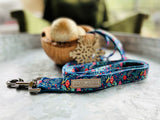 Dog wearing a blue holiday-themed Lucky Love Dog collar with festive ornament and foliage pattern outdoors.